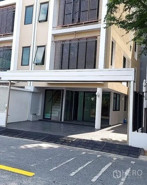 Home Office for rent in Huai Khwang, Bangkok - Ground-level view of the building’s covered parking and glass entry with sliding wood shutters.