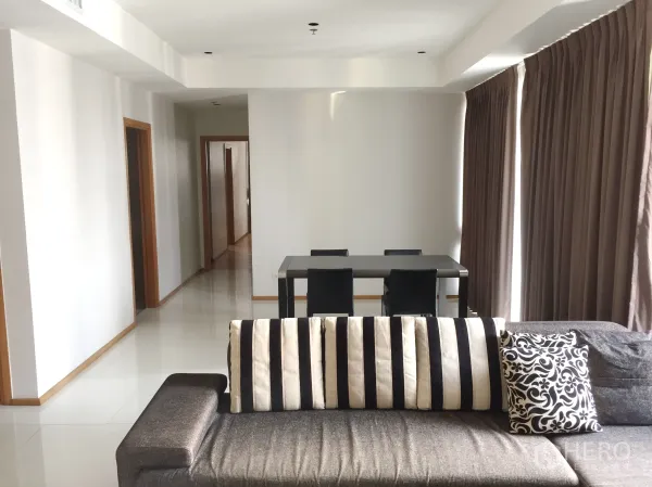 Condominium for rent in Khlong Toei, Bangkok - Spacious lounge with striped-cushion sofa, dining table for four, and hallway leading to bedrooms.