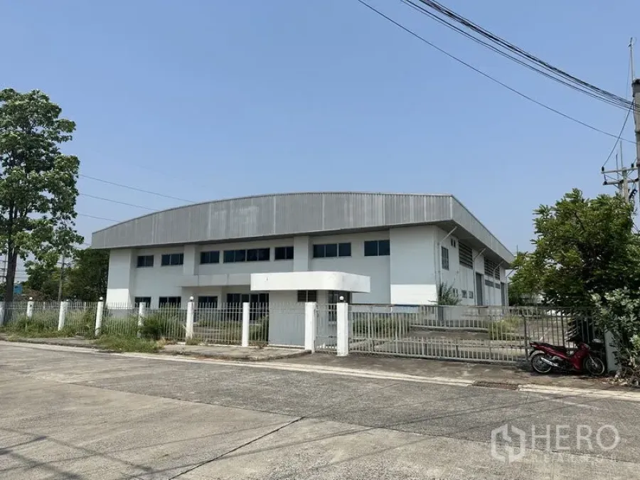 工厂 出租在Chon Buri - 工业园区内白色现代化工厂外观，弧形金属屋顶，围栏与大门清晰可见。