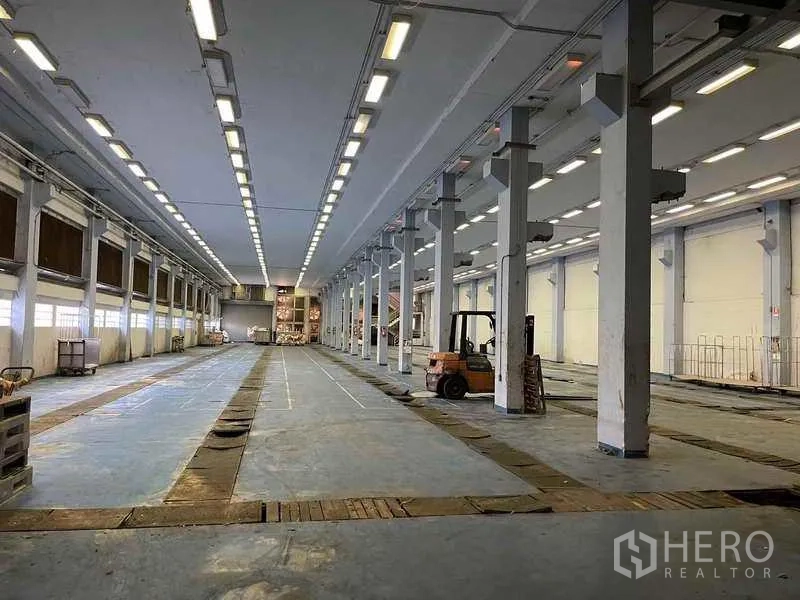 Factory for rent in Phra Samut Chedi, Samut Prakan - Rear driveway leading to a roller door and service building beside landscaped edges.
