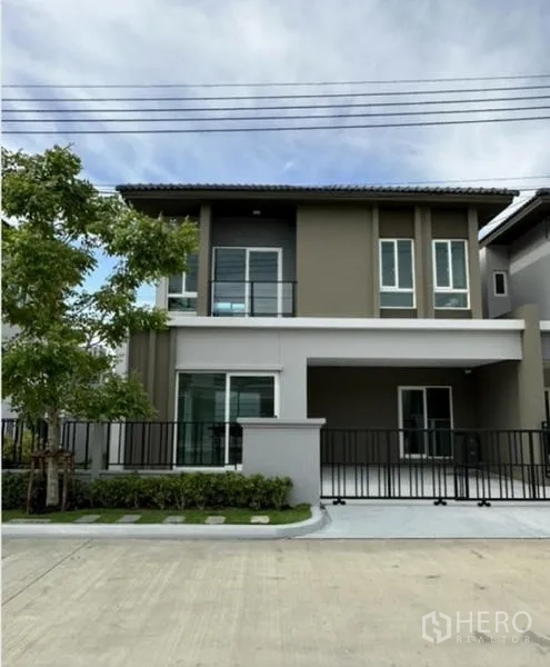 Townhouse for rent in Bang Phli, Samut Prakan - Front elevation of the townhouse with driveway, fence and greenery.