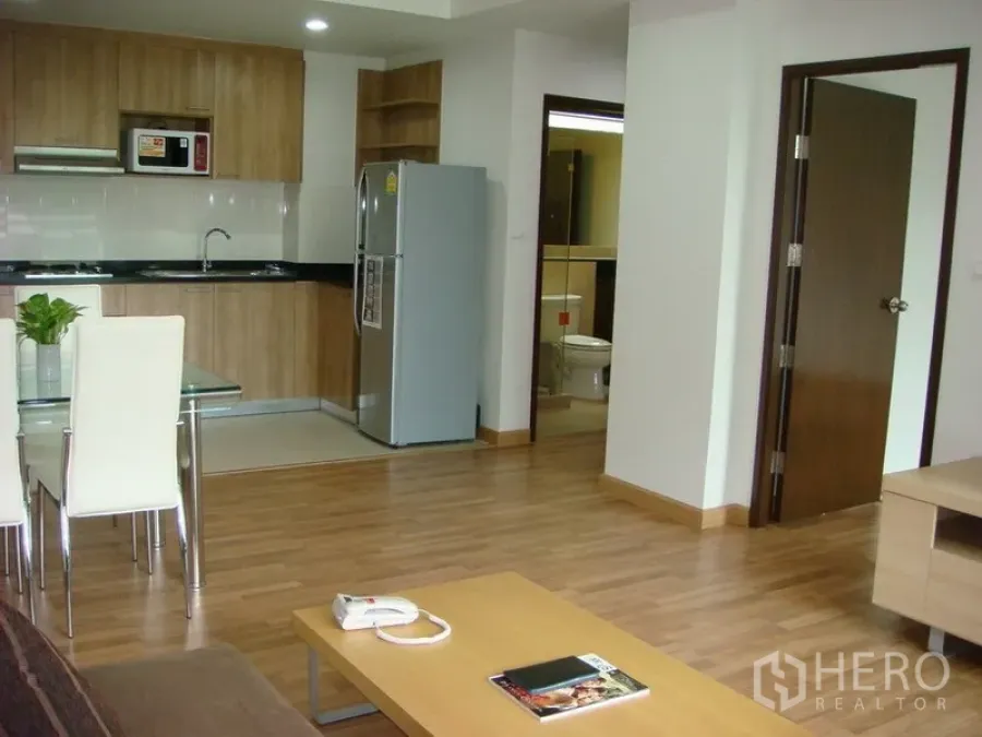 Apartment for rent in Khlong Toei, Bangkok - Open-plan living area in Asok apartment with wood floors, fitted kitchen with fridge and microwave, and a glass dining table.