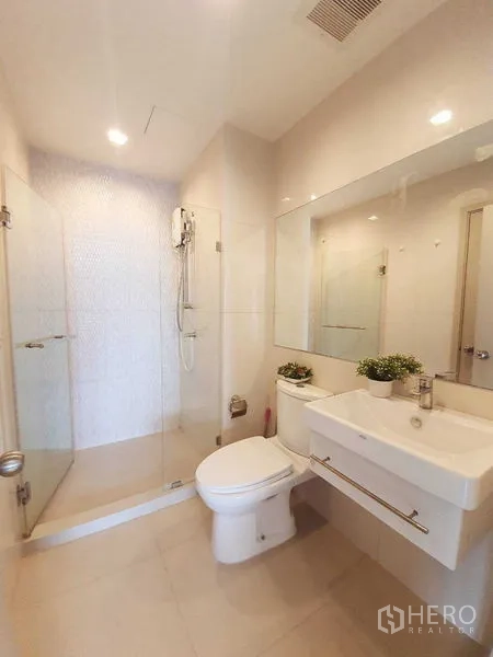 Condominium for sale in Khlong Toei, Bangkok - Modern bathroom with glass shower enclosure, large mirror, and white tiling.
