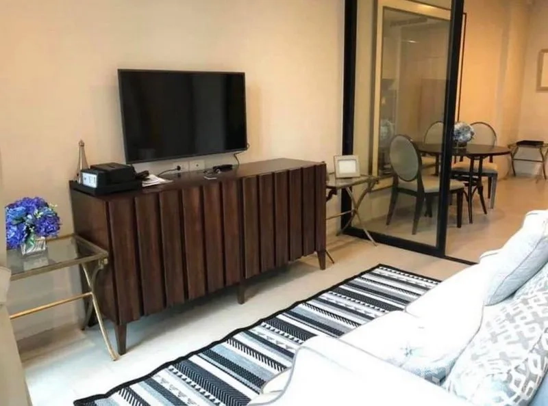 Condominium for rent in Pathum Wan, Bangkok - Living area with TV on a wooden console, striped rug, and a glass partition to the dining room.
