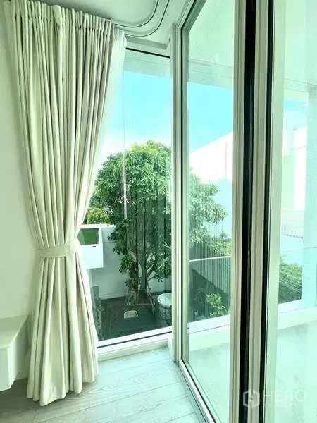 Detached House for rent or sale in Bang Phli, Samut Prakan - Floor-to-ceiling window with light curtains looking out to a green courtyard.