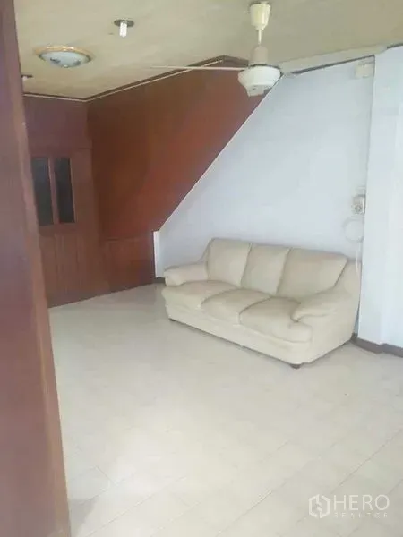 Townhouse for rent - Bright living area with cream sofa, tiled floor, and wood paneling under the stairs.