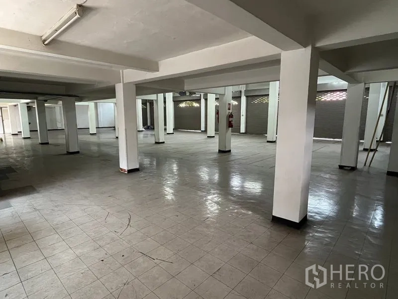 Shophouse for rent in Khlong Toei, Bangkok - Spacious tiled lower floor with multiple shuttered shop bays and sturdy support columns.