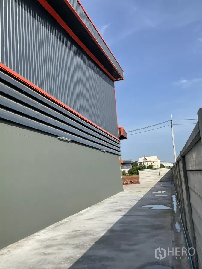 Factory for sale in Samut Sakhon - Distant street view of the factory building behind a perimeter fence on an open plot.