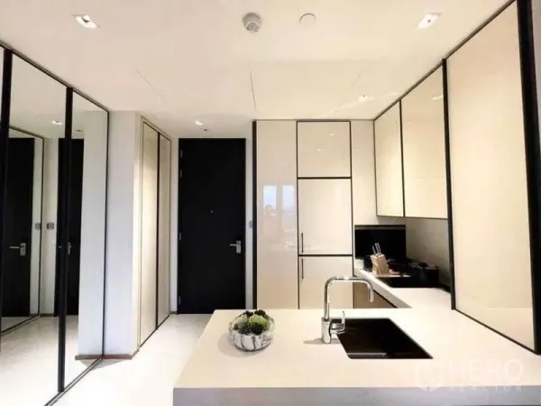 Condominium for rent or sale in Khlong Toei, Bangkok - Sleek white kitchen with island sink, built-in cabinets, and mirrored storage.
