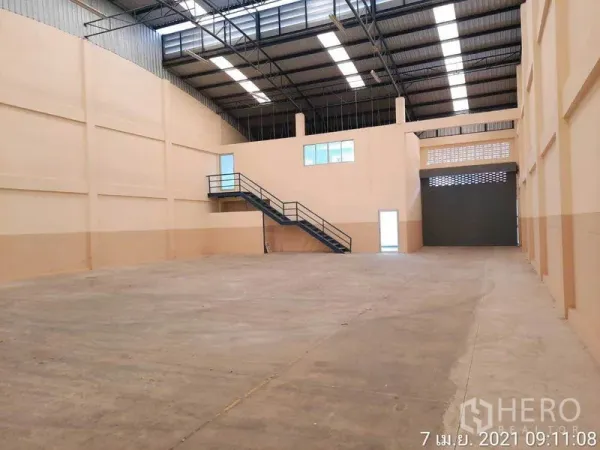 工厂 出租在Bang Bua Thong, Nonthaburi - 仓库内部空间开阔，高钢结构屋顶、采光带、夹层办公室与卷帘门。