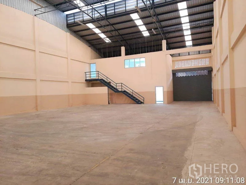 工厂 出租在Bang Bua Thong, Nonthaburi - 仓库内部空间开阔，高钢结构屋顶、采光带、夹层办公室与卷帘门。