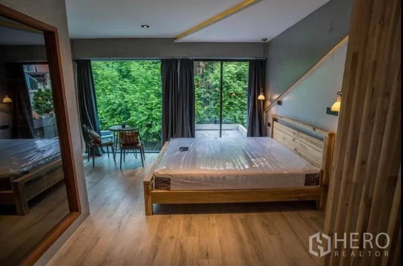 Townhouse for rent in Khlong Toei, Bangkok - Bedroom with wooden bed, floor-to-ceiling windows, balcony seating and leafy view.
