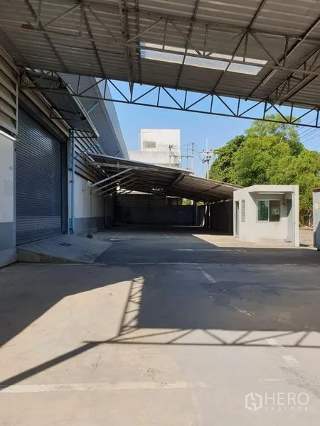 Warehouse for rent in Lam Luk Ka, Pathum Thani - Covered loading bay with roller shutters, guard booth, and spacious concrete yard.
