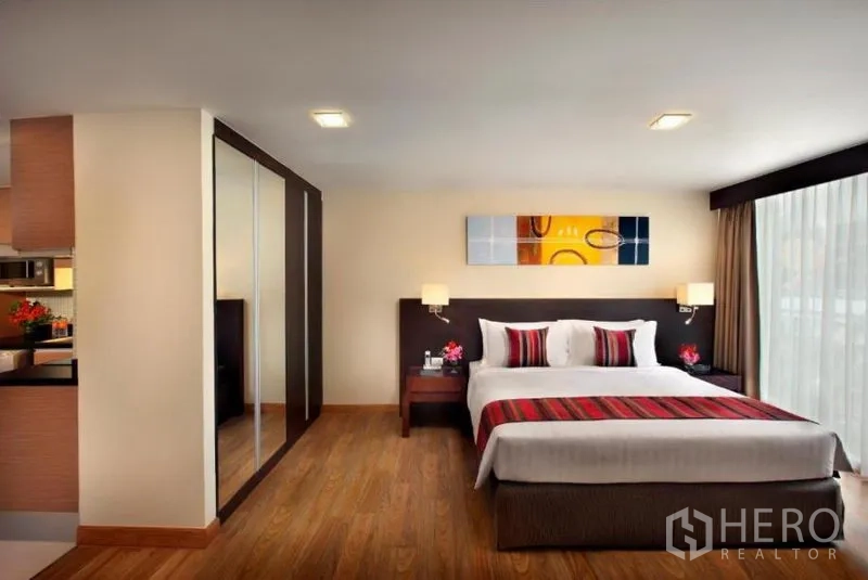 Condominium for rent in Khlong Toei, Bangkok - Spacious bedroom with king bed, wood floors, mirrored wardrobe and large window.