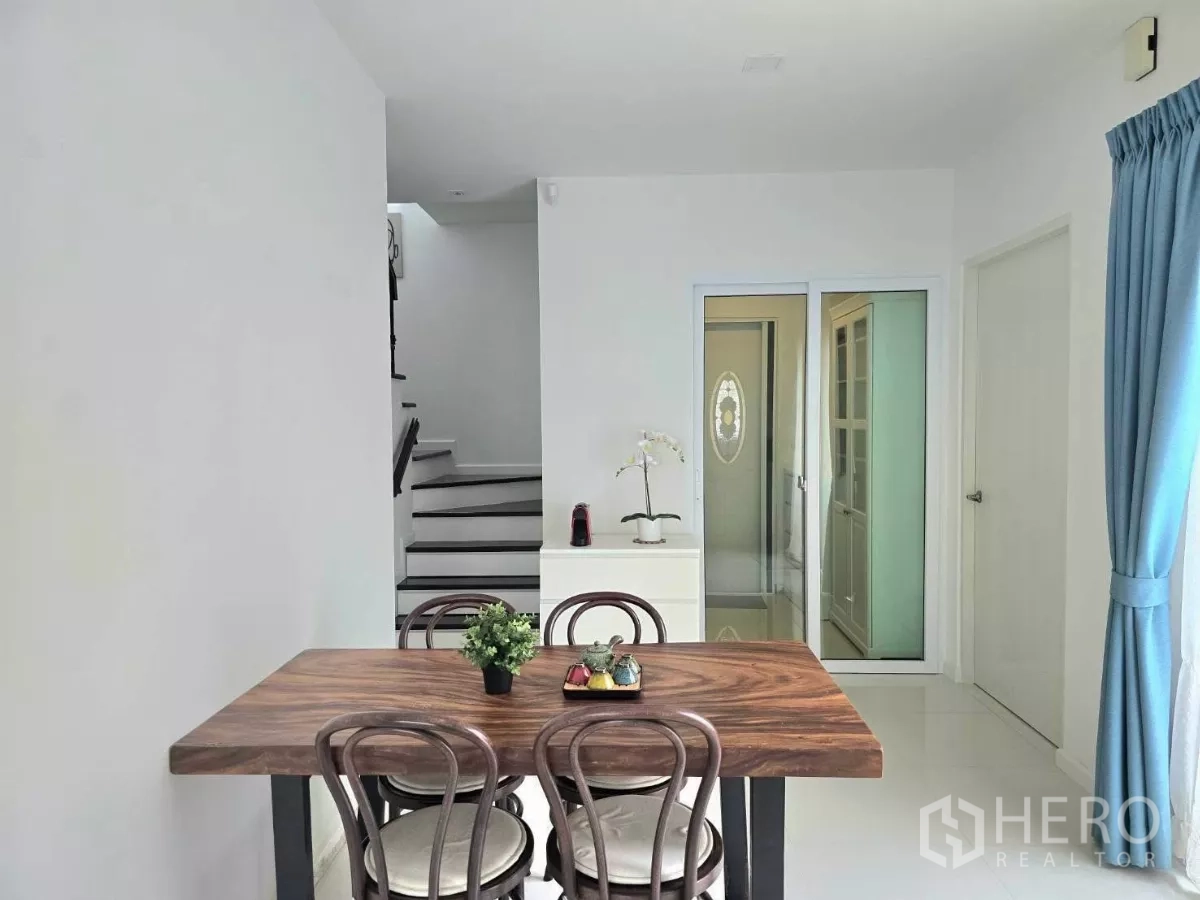 Detached House for rent in Samut Prakan - Open-plan dining space with wood table, staircase and glass doors to the kitchen.