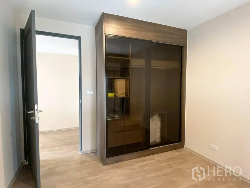Condominium for rent in Pathum Wan, Bangkok - Second bedroom featuring a dark glass sliding-door wardrobe and wood flooring.