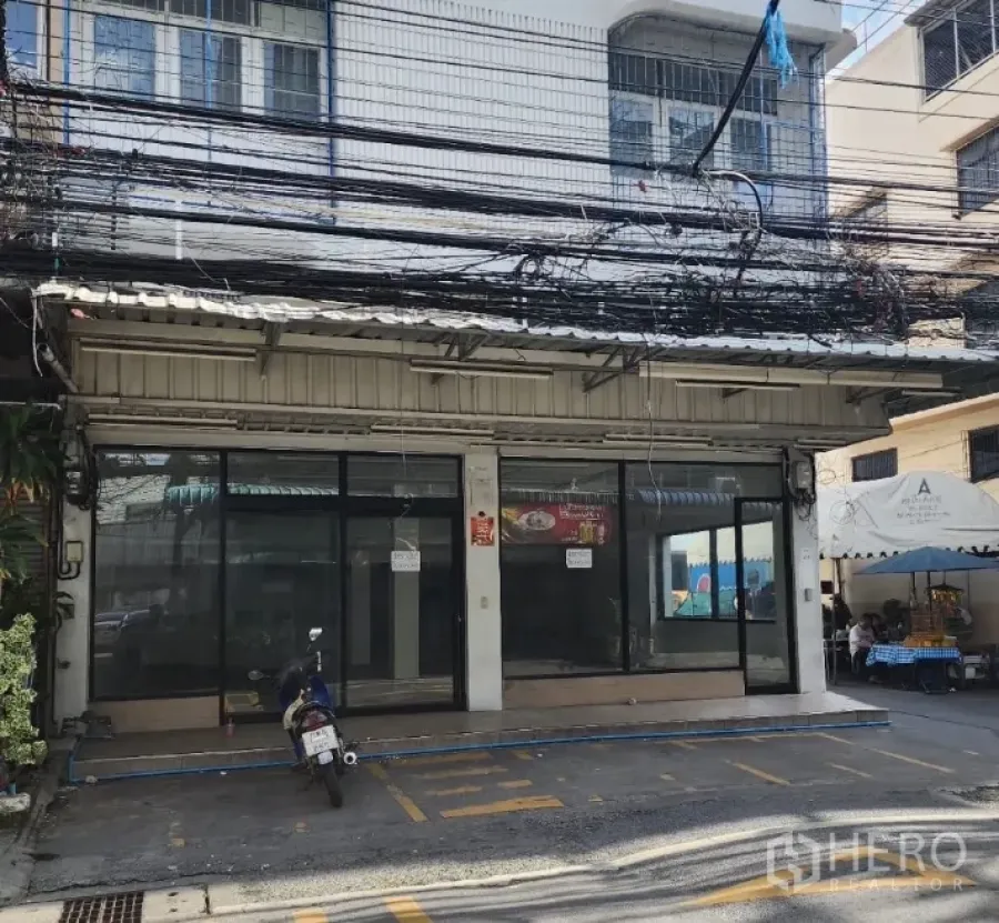 Retail Space for rent in Suan Luang, Bangkok - Street-level retail frontage with full glass windows and parking markings in a Bangkok neighborhood.
