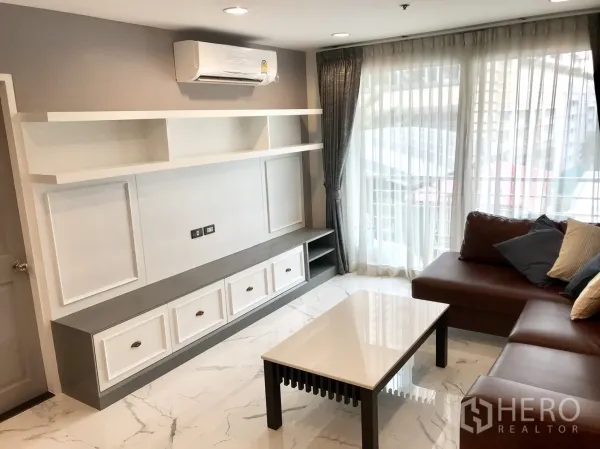 Condominium for rent or sale in Khlong Toei, Bangkok - Built-in TV console with open shelves and air-conditioning beside a sofa and floor-to-ceiling windows.