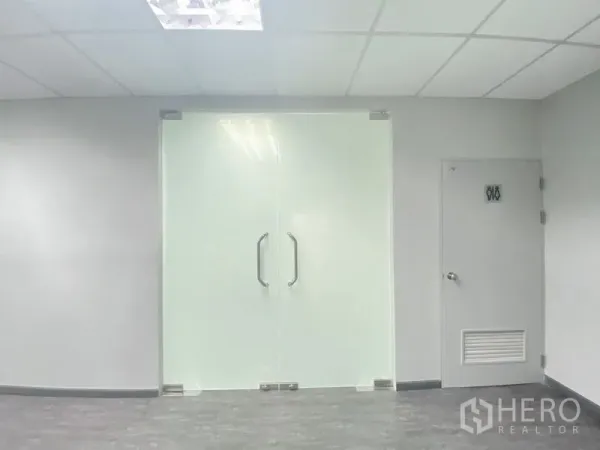 Office Space for rent in Chatuchak, Bangkok - Close-up of frosted glass double doors and a service door along a corridor with grey flooring.