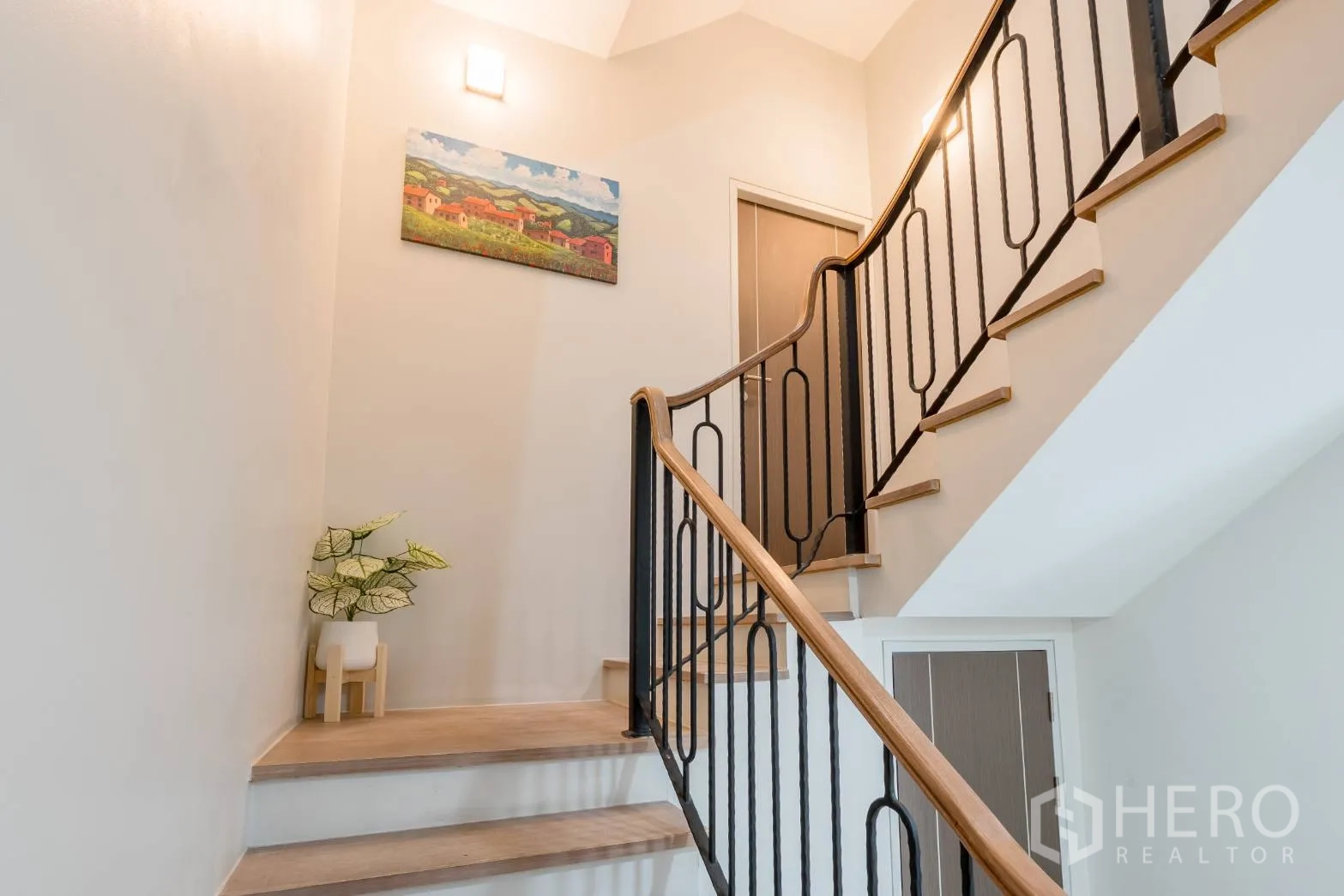 Home Office for rent in Khlong Toei, Bangkok - Staircase with black iron balustrade and wood handrail under warm wall lights.