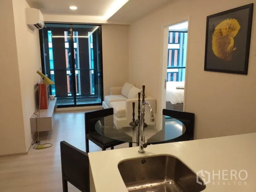 Condominium for rent in Khlong Toei, Bangkok - Open-plan living area with white sofa, balcony doors, and a kitchen island in a modern condo near BTS Thonglor.
