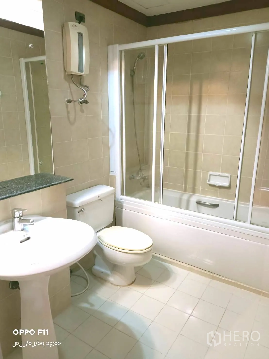 Condominium for rent in Khlong Toei, Bangkok - Tiled bathroom with bathtub and sliding shower screen, pedestal sink and toilet.