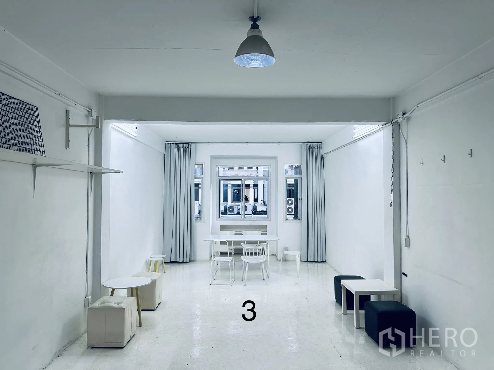 Shophouse for rent in Watthana, Bangkok - Long white room with cube seating, small tables, a central window, and a ceiling light.