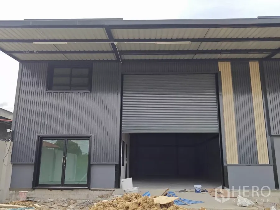 Warehouse for rent in Sam Phran, Nakhon Pathom - Close-up of the warehouse frontage showing a large roller shutter door and a glass office entrance.