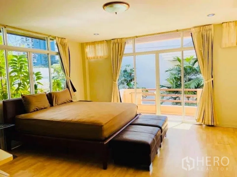 Detached House for rent in Watthana, Bangkok - Sunlit master bedroom with king bed, balcony access and floor-to-ceiling windows overlooking greenery.