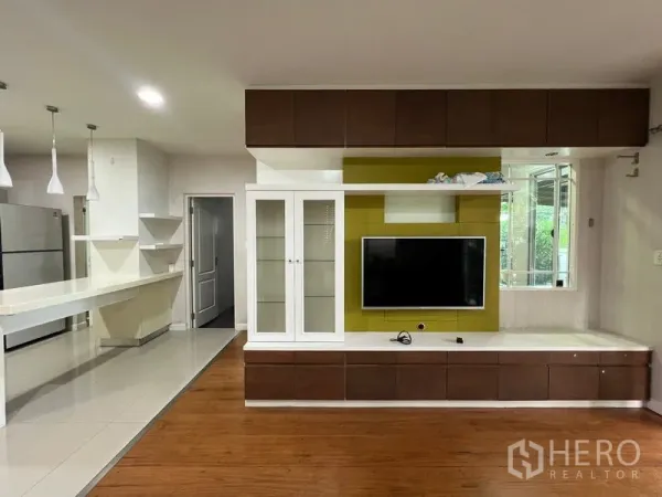 Detached House for rent in Bang Kapi, Bangkok - Open-plan living area with TV feature wall, built-in cabinets and an adjacent pantry kitchen with island.