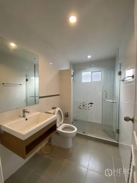 Detached House for rent in Suan Luang, Bangkok - Bathroom with glass-enclosed shower, wall mirror and modern sanitary ware.