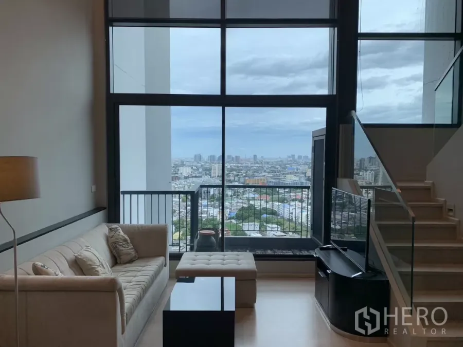 Condominium for rent in Khlong Toei, Bangkok - Sofa and TV facing tall windows opening to a balcony with wide Bangkok city skyline views.