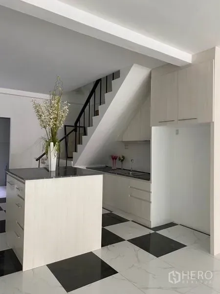 Townhouse for rent or sale in Khlong Toei, Bangkok - White kitchen with black countertop island and storage under the stairs