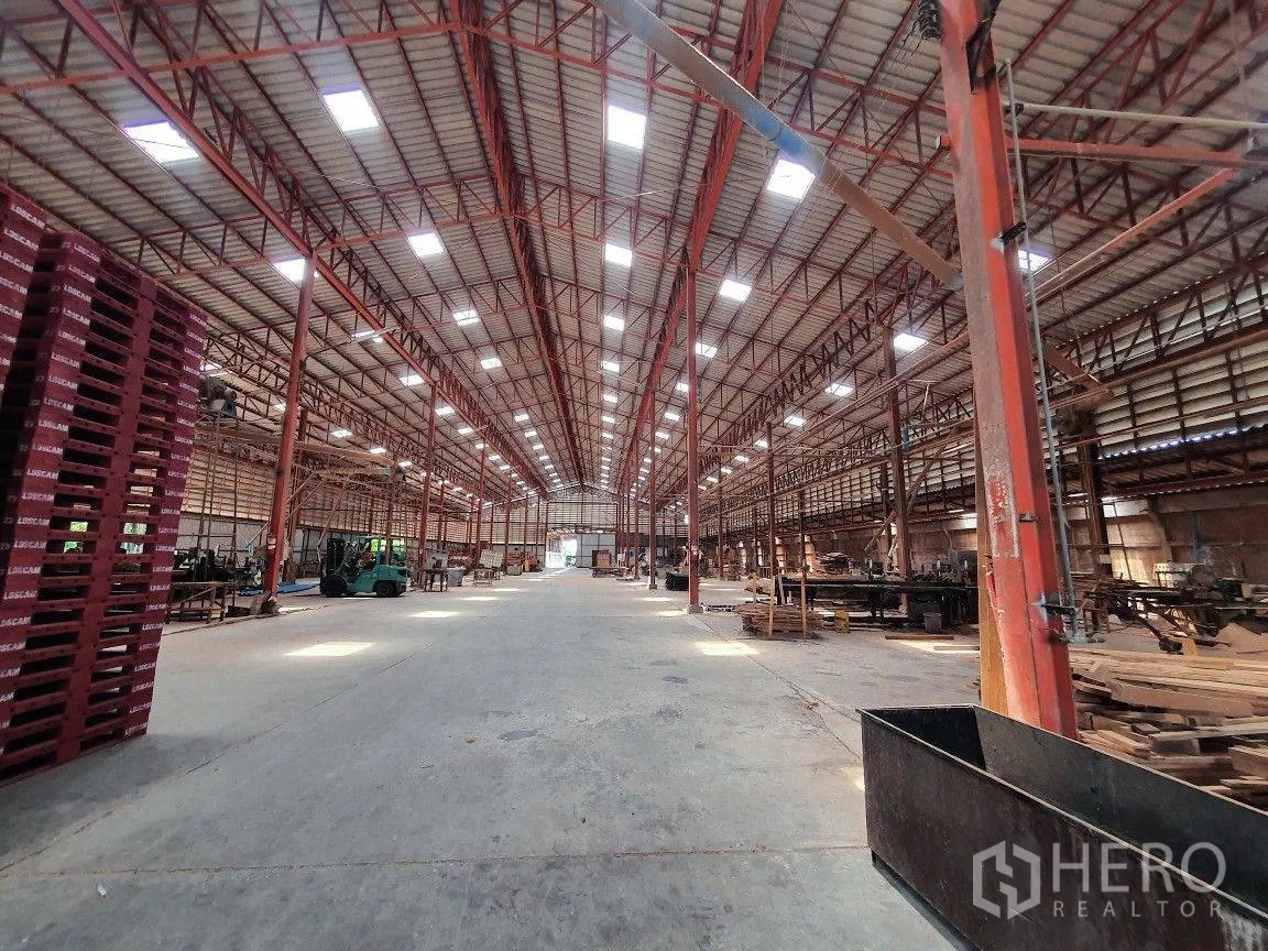Warehouse for rent in Lam Luk Ka, Pathum Thani - Wide central aisle inside the warehouse with skylights, red steel columns and forklifts.