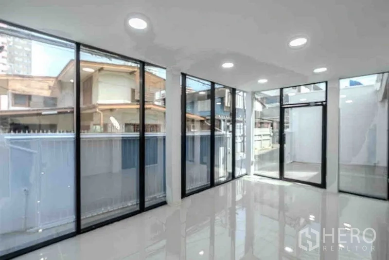 Standalone for rent or sale in Bang Na, Bangkok - Bright ground-floor showroom with floor-to-ceiling windows and glossy white tiled flooring.