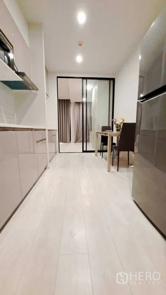 Condominium for rent or sale in Pathum Wan, Bangkok - Galley kitchen view toward glass partition and dining table, with wood flooring throughout.