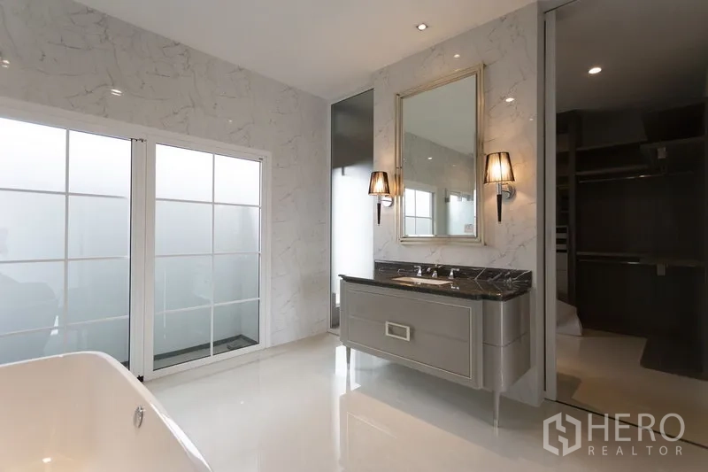 Detached House for rent in Mueang Samut Prakan, Samut Prakan - Luxury bathroom with marble-effect walls, double vanity, bathtub and frosted glass doors.
