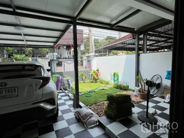 Townhouse for rent in Din Daeng, Bangkok - Covered carport with checkerboard floor beside a small landscaped front garden and gate.