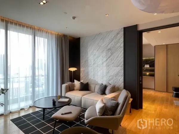 Condominium for rent in Khlong Toei, Bangkok - Sofa against a marble feature wall with sheer curtains and a round coffee table.