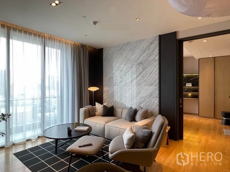 Condominium for rent in Khlong Toei, Bangkok - Sofa against a marble feature wall with sheer curtains and a round coffee table.