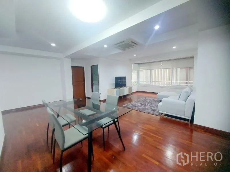 Condominium for rent in Watthana, Bangkok - Open-plan living and dining area with glass table, white sofa, TV console and polished hardwood floors.