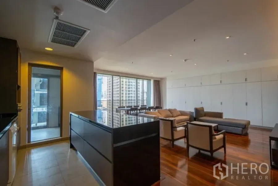Condominium for rent in Khlong Toei, Bangkok - Open‑plan living and dining with an island kitchen, hardwood floors, floor‑to‑ceiling windows and city view.