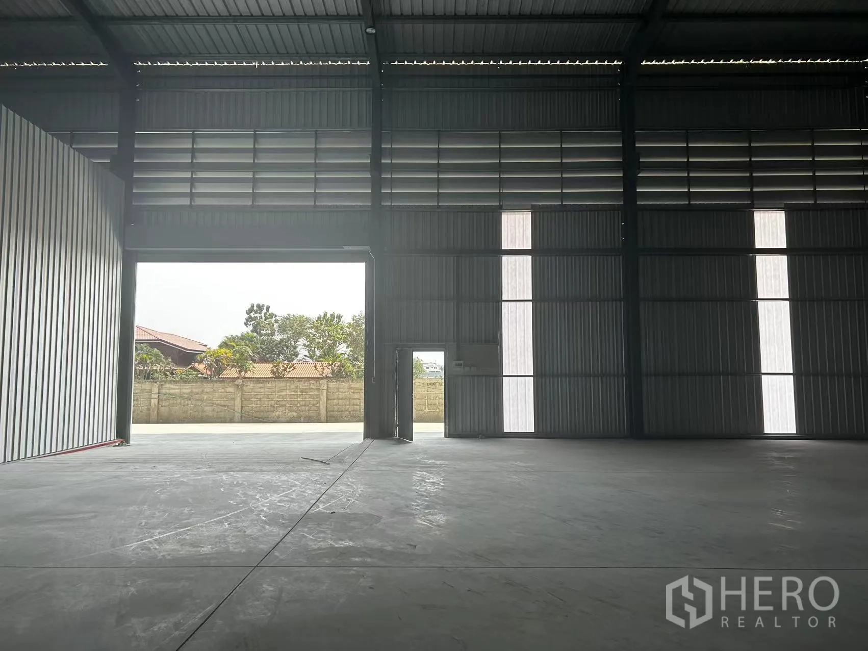 Warehouse for rent in Lam Luk Ka, Pathum Thani - Interior view facing the wide entrance opening to the paved yard and boundary wall.