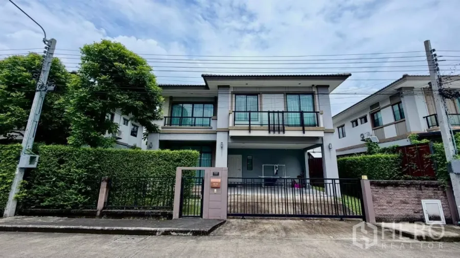 Detached House for rent or sale in Bang Phli, Samut Prakan - Street view of a modern two-storey detached house with gated driveway and trimmed hedges in Bang Phli.