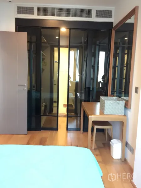 Condominium for rent in Khlong Toei, Bangkok - Bedroom with glass wardrobe doors, a dressing desk and warm wooden flooring.