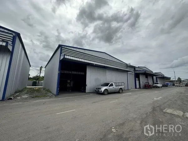 Warehouse for rent in Khlong Luang, Pathum Thani - Row of steel-clad warehouses with wide loading bays and parking along an access road in Khlong Luang, Pathum Thani.