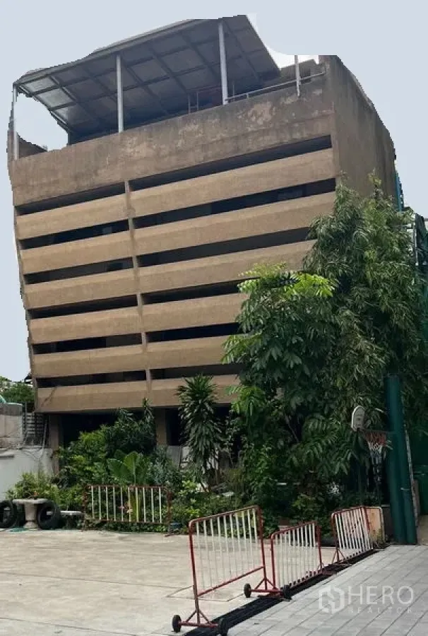 Retail Space for rent in Khlong Toei, Bangkok - Mid-rise concrete building with horizontal facade slats, rooftop canopy, and an open courtyard with greenery and safety barriers in Khlong Toei, Bangkok.