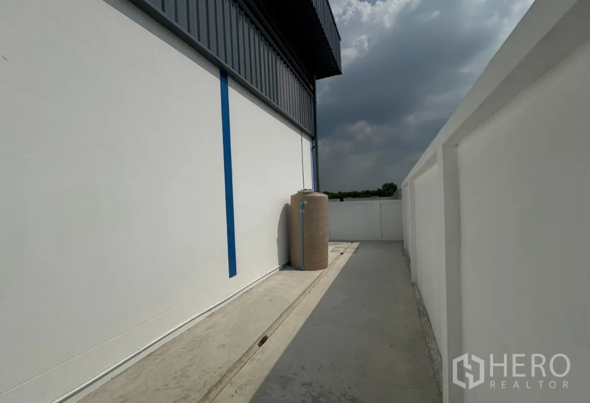 Warehouse for rent in Khlong Luang, Pathum Thani - Side service walkway with water storage tank and boundary wall.