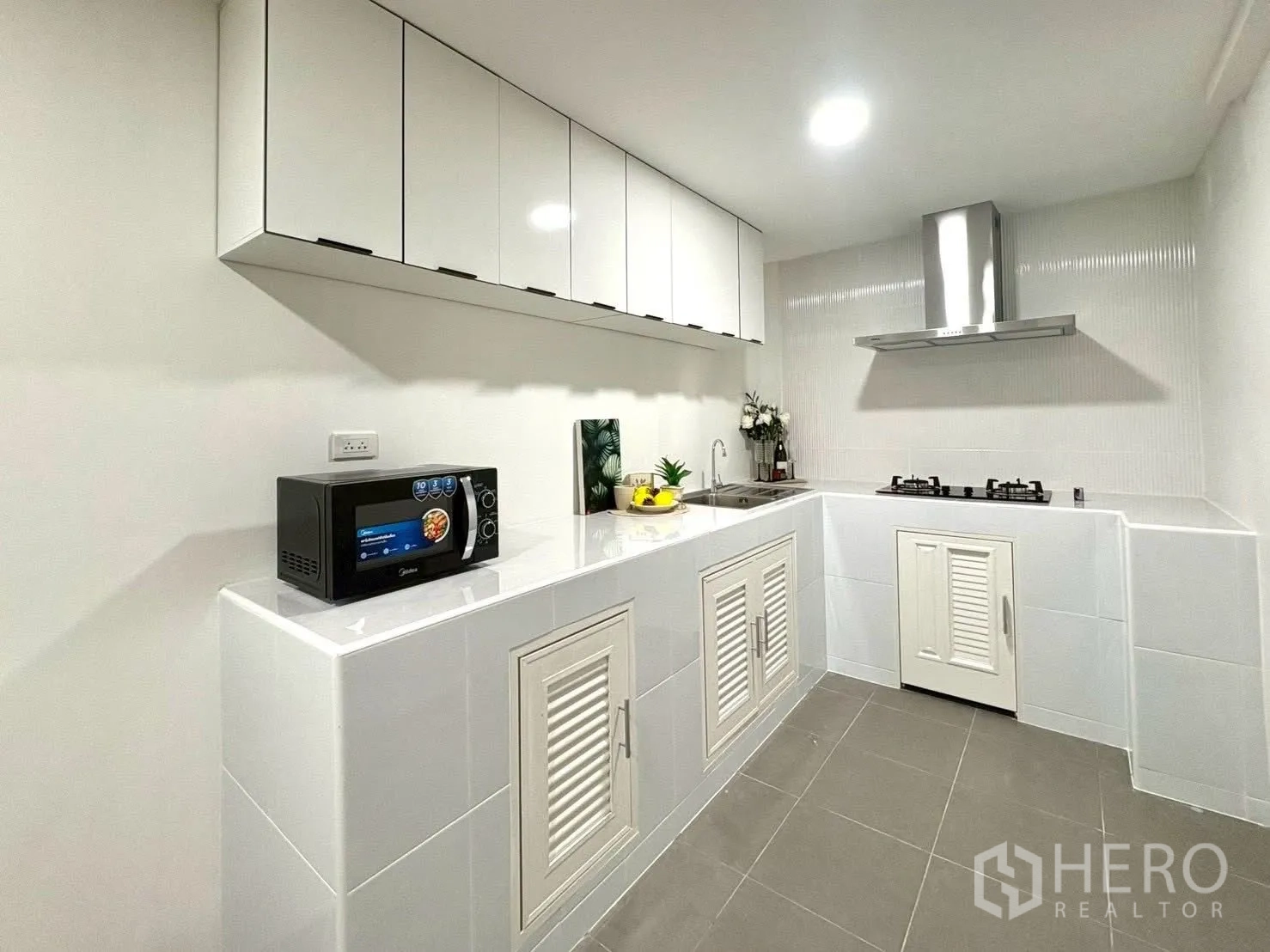 Townhouse for rent in Huai Khwang, Bangkok - White kitchen with cabinets, sink, microwave, and gas cooktop with hood.