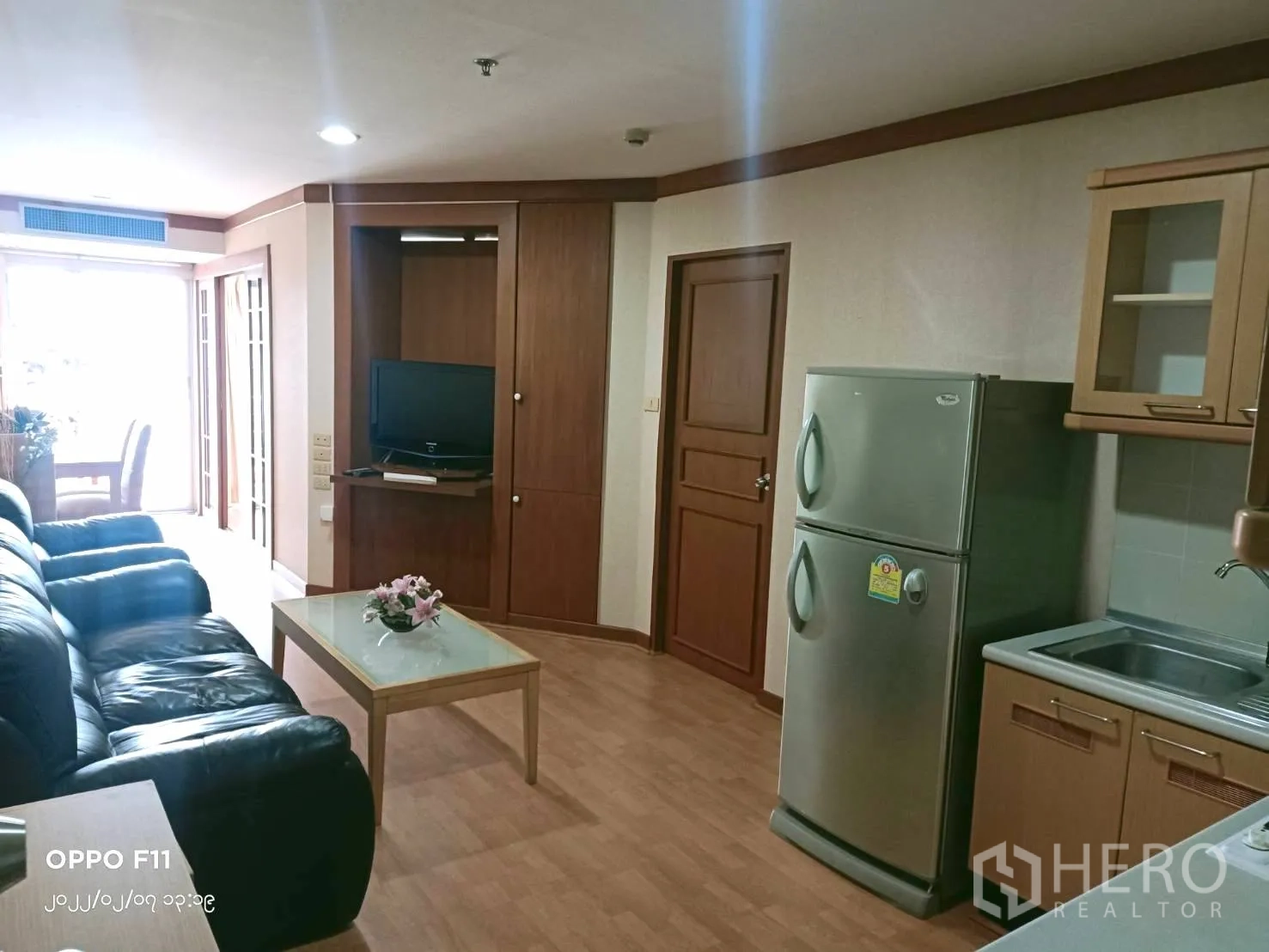 Condominium for rent in Khlong Toei, Bangkok - Kitchen and living area showing refrigerator, sink, TV cabinet and wood flooring.
